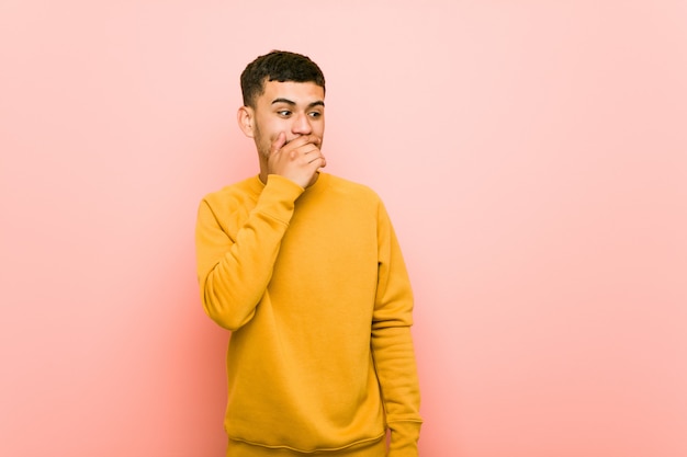 Young hispanic man thoughtful looking to a copy space covering mouth with hand.