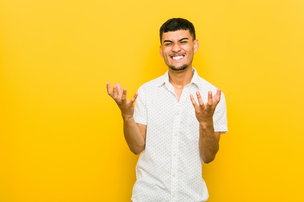 Young hispanic man upset screaming with tense hands