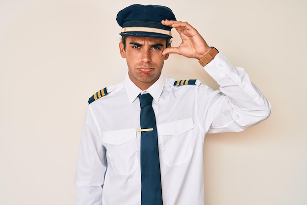 Young hispanic man wearing airplane pilot uniform worried and stressed about a problem with hand on forehead, nervous and anxious for crisis