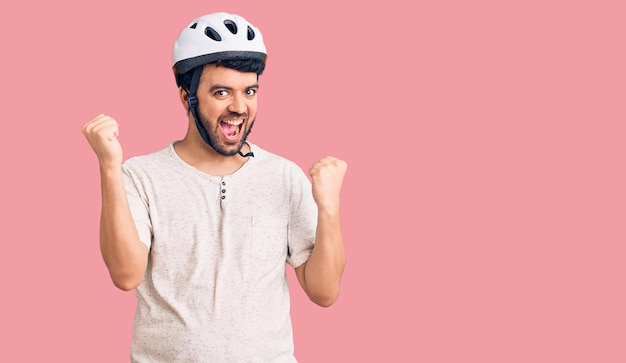 Young hispanic man wearing bike helmet screaming proud, celebrating victory and success very excited with raised arms