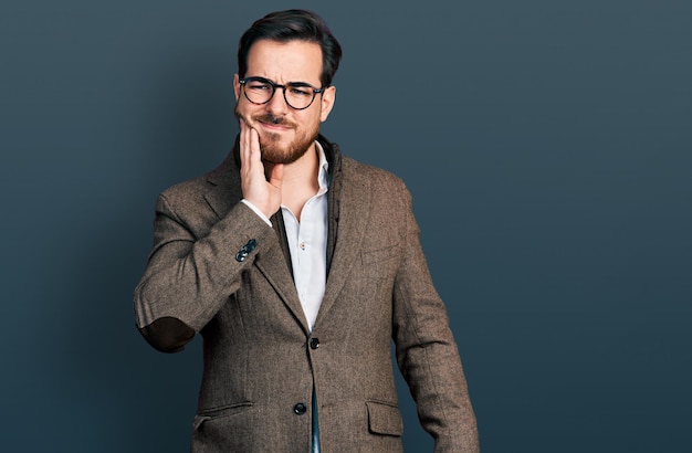 Young hispanic man wearing business jacket and glasses touching mouth with hand with painful expression because of toothache or dental illness on teeth dentist