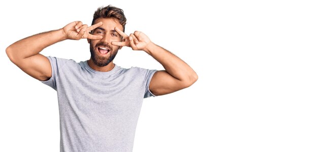 Young hispanic man wearing casual clothes doing peace symbol with fingers over face, smiling cheerful showing victory