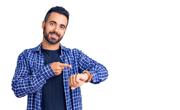 Young hispanic man wearing casual clothes in hurry pointing to watch time impatience upset and angry for deadline delay