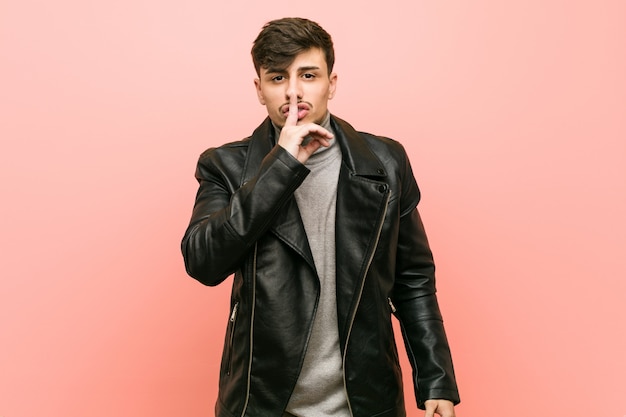 Young hispanic man wearing a leather jacket keeping a secret or asking for silence.