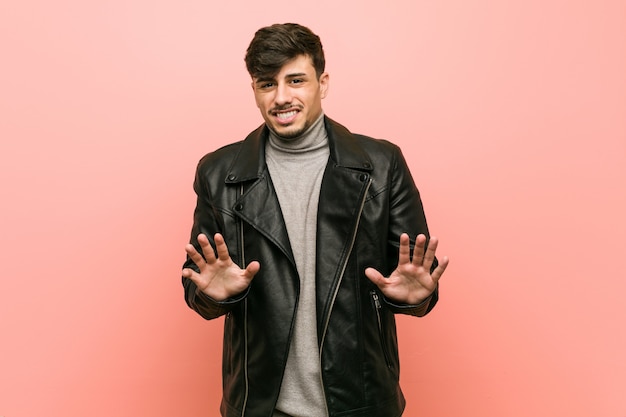 Young hispanic man wearing a leather jacket rejecting someone showing a gesture of disgust.