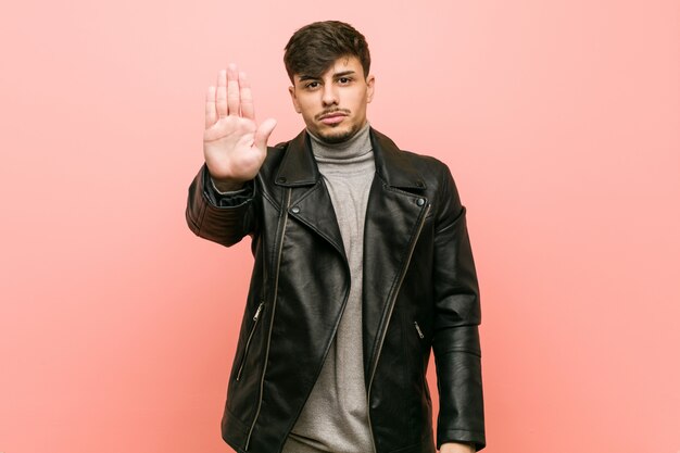 Young hispanic man wearing a leather jacket standing with outstretched hand showing stop sign, preventing you.