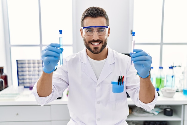 Young hispanic man wearing scientist uniform holding test tube at laboratory