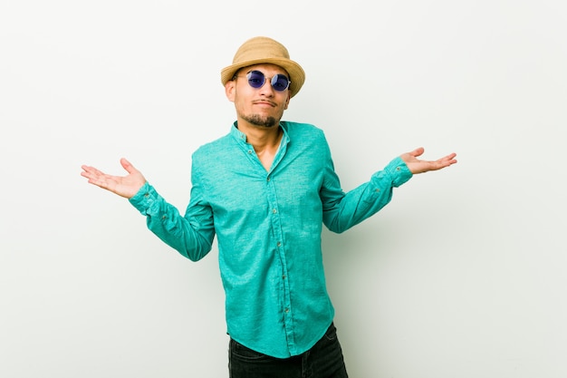 Young hispanic man wearing a summer clothes confused and doubtful shrugging shoulders to hold a copy space