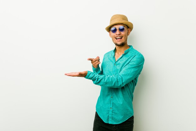 Young hispanic man wearing a summer clothes excited holding a blank space on palm.