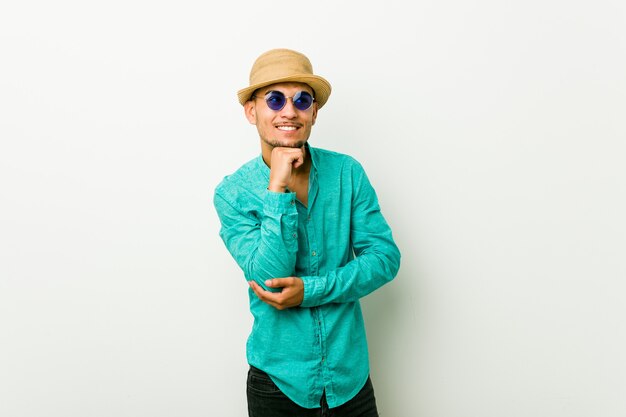 Young hispanic man wearing a summer clothes keeps hands under chin