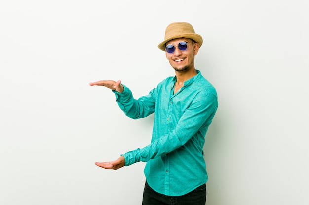 Young hispanic man wearing a summer clothes shocked and amazed holding a copy space between hands.