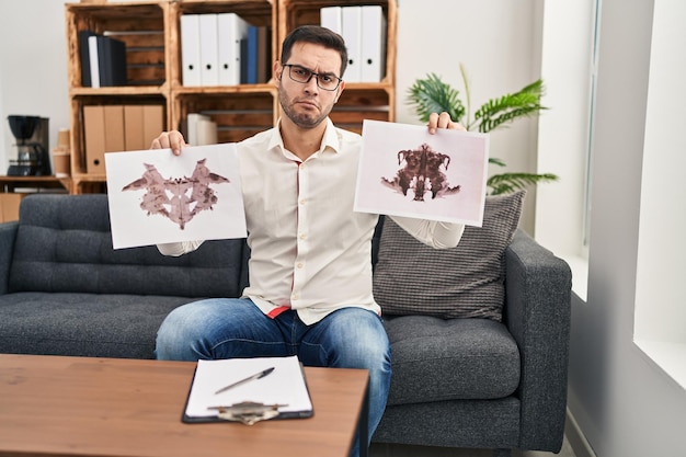 Young hispanic man with beard holding rorschach test depressed and worry for distress crying angry and afraid sad expression