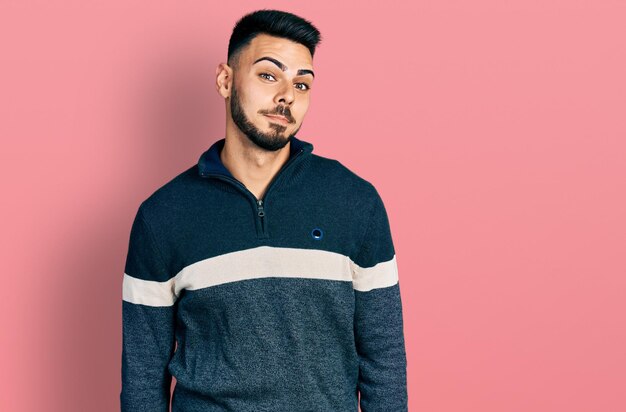 Foto giovane uomo ispanico con la barba che indossa un maglione invernale casual che sorride guardando di lato e fissando il pensiero