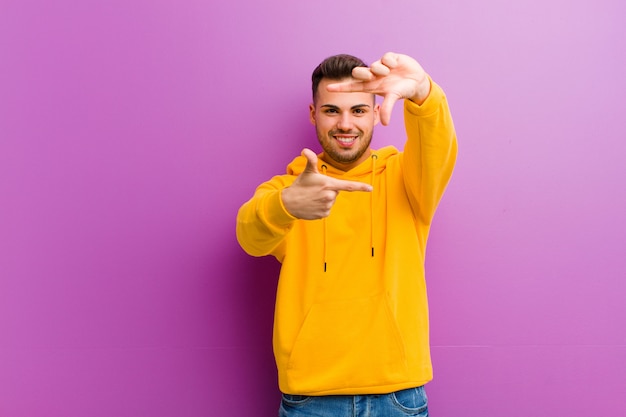 Young hispanic man with casual look against purple wall