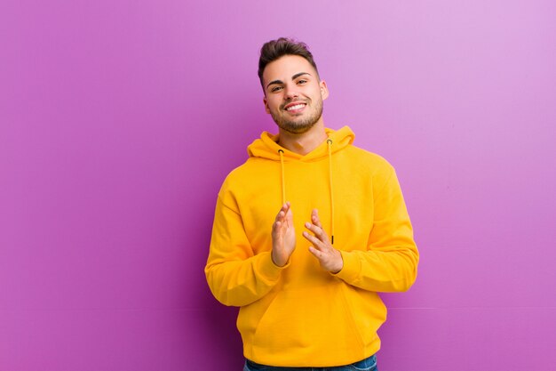 Young hispanic man with casual look against purple wall