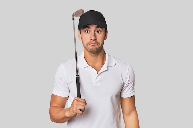 Foto giovane ispanico con un mazzo da golf si alza le spalle e gli occhi aperti confusi