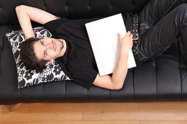 A young hispanic man with a laptop on the Sofa.