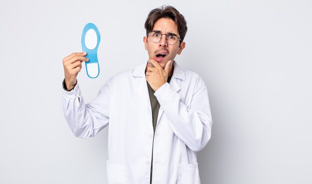 Young hispanic man with mouth and eyes wide open and hand on chin. chiropodist concept