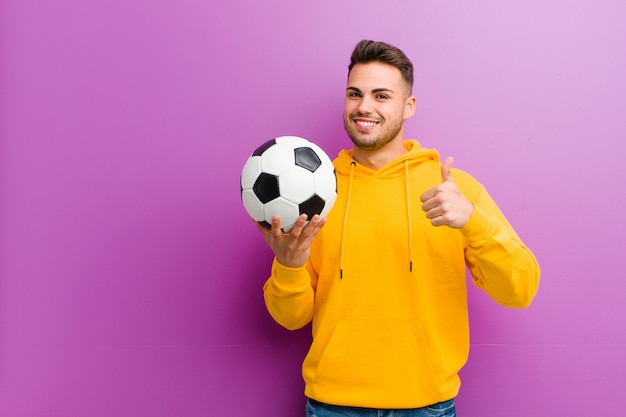 Young hispanic man with a soccer ball against purple 