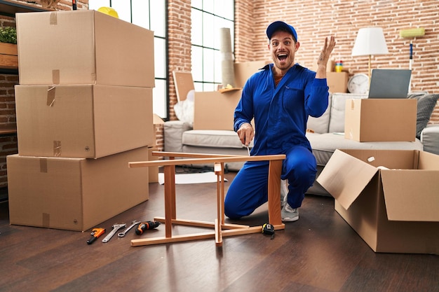 Young hispanic man working on moving service celebrating victory with happy smile and winner expression with raised hands