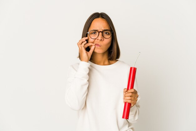 Young hispanic mixed race woman holding a dynamite with fingers on lips keeping a secret.