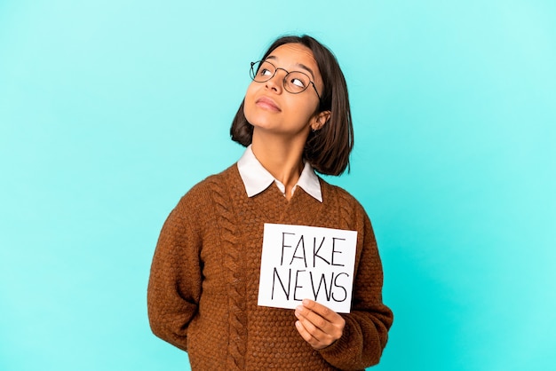 Young hispanic mixed race woman holding a fake news placard dreaming