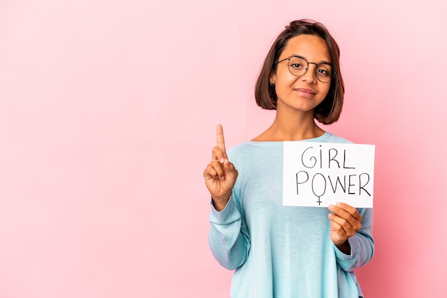 Young hispanic mixed race woman holding a girl power message placard showing number one with finger.