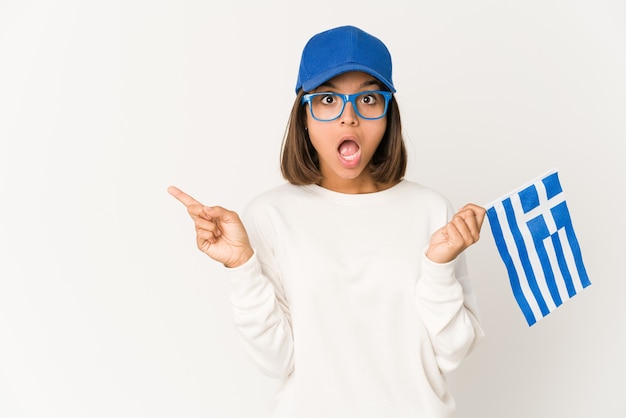 Young hispanic mixed race woman holding a greece flag pointing to the side