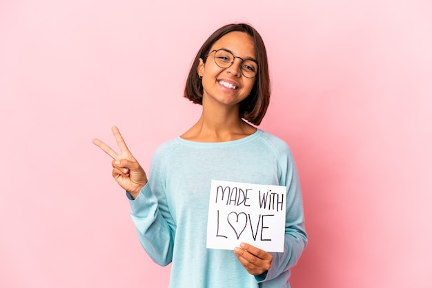 Young hispanic mixed race woman holding a made with love paper poster joyful and carefree showing a peace symbol with fingers.