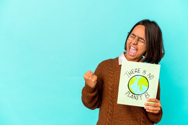 Young hispanic mixed race woman holding a planet save placard raising fist after a victory, winner concept.