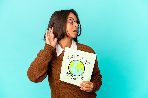 Young hispanic mixed race woman holding a planet save placard trying to listening a gossip.