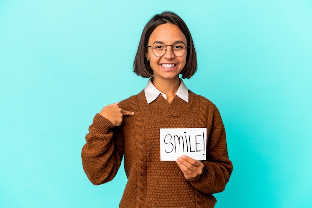 Young hispanic mixed race woman holding a smile note person pointing by hand to a shirt copy space, proud and confident