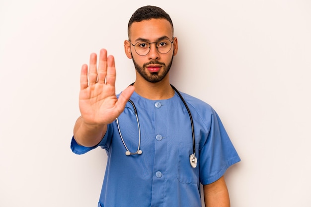 Young hispanic nurse man isolated on white background standing with outstretched hand showing stop sign preventing you