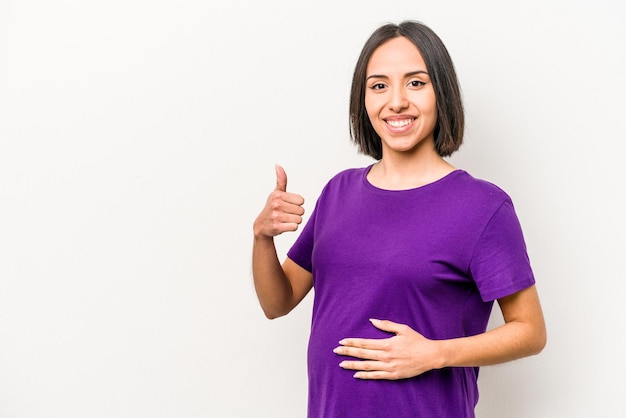 Молодая латиноамериканская беременная женщина изолирована на белом фоне, улыбаясь и поднимая большой палец вверх