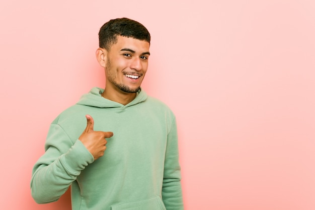 Young hispanic sport man person pointing by hand to a shirt copy space, proud and confident