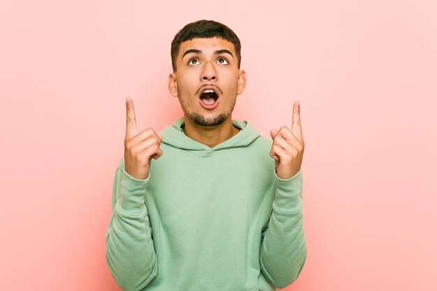 Young hispanic sport man pointing upside with opened mouth.