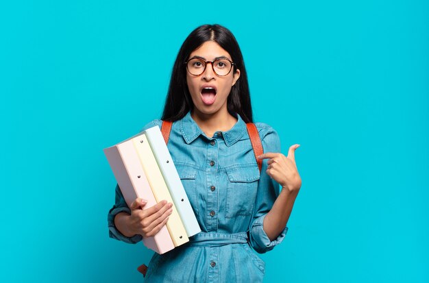 Young hispanic student woman feeling happy, surprised and proud, pointing to self with an excited, amazed look