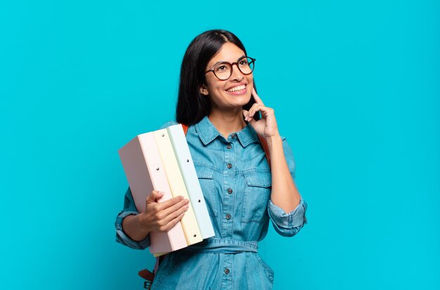 Giovane donna ispanica studentessa sorridente felicemente e fantasticando o dubitando, guardando al lato