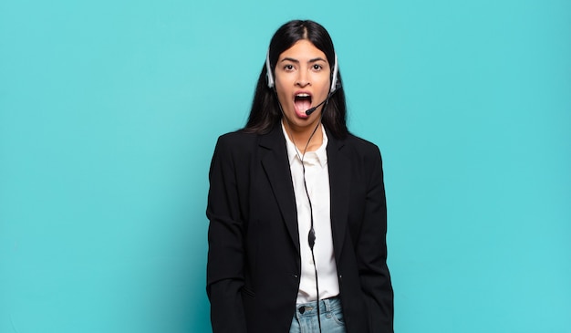 Young hispanic telemarketer woman looking very shocked or surprised