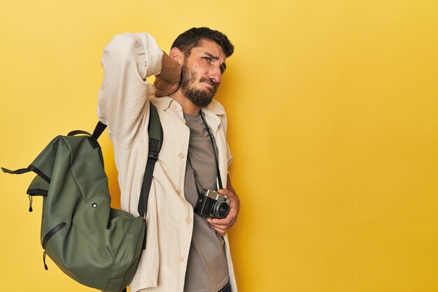 Photo young hispanic travel photographer poses touching back of head thinking and making a choice