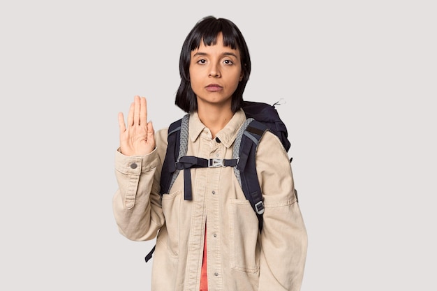 Young Hispanic with trekking backpack ready showing number one with finger