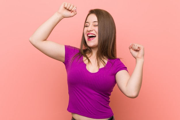 Young hispanic woman against a pink wall celebrating a special day, jumps and raise arms with energy.