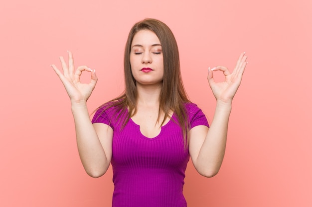 Giovane donna ispanica contro un muro rosa si rilassa dopo una dura giornata di lavoro, sta eseguendo yoga.