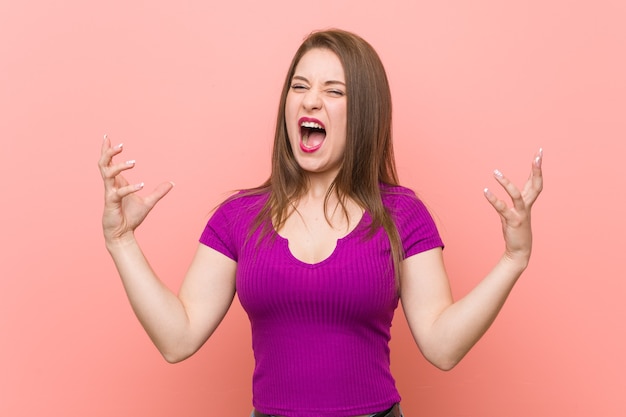 Young hispanic woman against a pink wall screaming with rage.