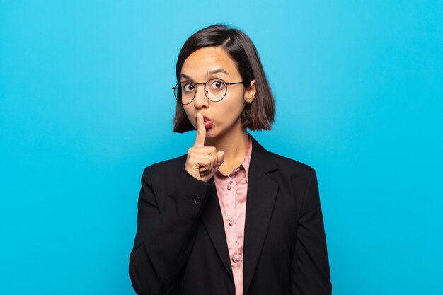 Young hispanic woman asking for silence and quiet, gesturing with finger in front of mouth, saying shh or keeping a secret