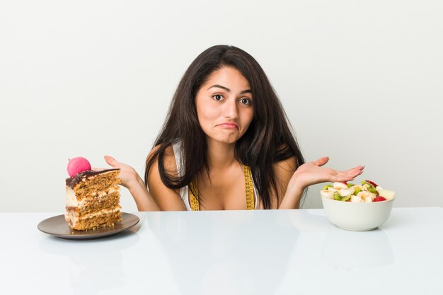 Giovane donna ispanica che sceglie fra il dolce o la ciotola di frutta