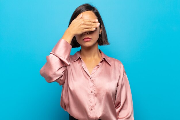 Young hispanic woman covering eyes with one hand feeling scared or anxious, wondering or blindly waiting for a surprise