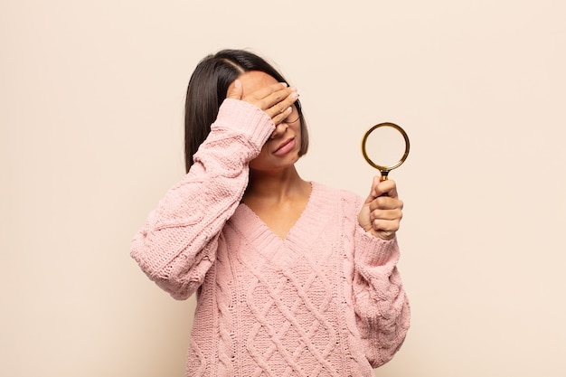 Young hispanic woman covering face with hand and putting other hand up front to stop camera, refusing photos or pictures