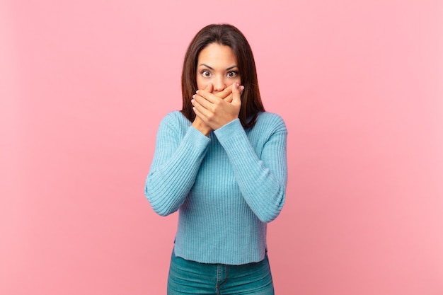 Young hispanic woman covering mouth with hands with a shocked