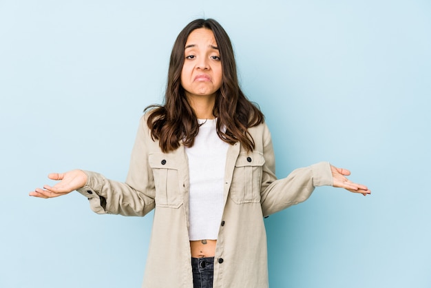 Young hispanic woman doubting and shrugging shoulders in questioning gesture.